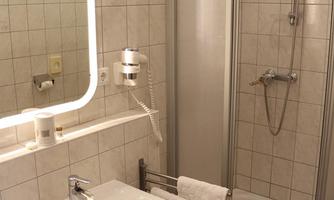 A modern bathroom with a shower and a sink. The walls are tiled and there is a large mirror.