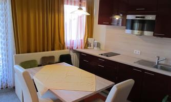 A modern kitchen with a dining table and several chairs. The walls are designed in warm tones, and large windows let in a lot of light.