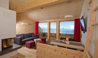 A modern living room with wood paneling and large windows. There is a cozy sofa, a table, and a fireplace that creates a warm atmosphere.