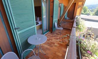A cozy balcony with two chairs and a table. The shutters are green and offer a view of the surroundings.