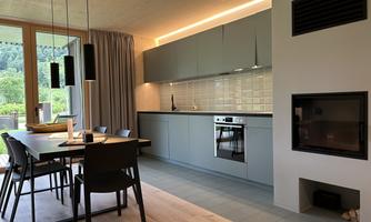 A modern kitchen with bright colors and a dining area. Large windows offer a view of the greenery.