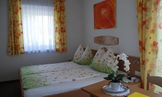 A cozy room with a double bed and cheerful, blooming curtains. An orchid is on the table and a TV is visible.