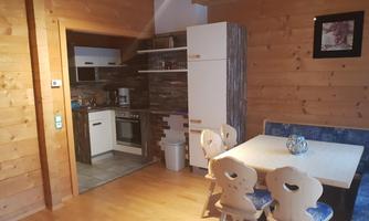 A cozy wooden apartment with a modern kitchenette and a dining area. The space has a warm, inviting character.