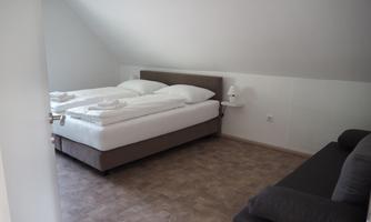 A bright bedroom with a double bed and a sofa bed. The furniture is modern and the walls are simply designed.