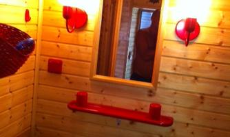A small bathroom with wooden walls and red accents. There is a sink, a mirror, and some lights.