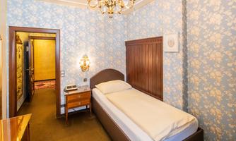 A simple single room with floral wallpaper and a wooden bed. A television and a bedside table are located next to the bed.