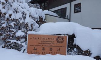 A sign reading "Apartments" in a snowy environment. The snow-covered landscape and the building in the background give the scene a cozy winter atmosphere.