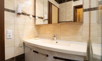 A modern bathroom with a white vanity and large mirrors. The walls are tiled in light colors, providing a clean, elegant atmosphere.