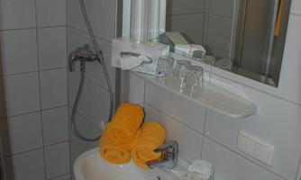 A small bathroom with a shower and a sink. Yellow towels are lying on the sink and the mirror is present.