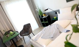 A modern bedroom with a double bed and a chair. The room is bright and welcoming, with large windows and stylish furniture.