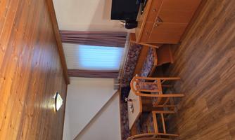 A cozy living and dining room with wooden floor. There is a table, chairs, and a television next to a kitchenette.
