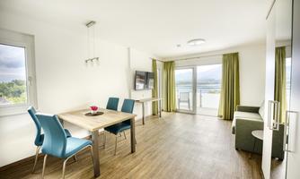 A modern apartment with a dining table and blue chairs. Large windows overlooking the landscape and bright, friendly colors.