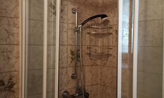 A shower cabin with transparent glass doors and a modern shower head. The walls are decorated with a light tile pattern.