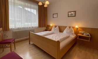 A cozy room with two single beds and light wood. Large windows allow plenty of light in, and the decor is simple and inviting.