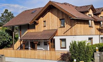 A modern wooden house with a well-kept front garden. The facade is clad in wood and the roof is covered in red.