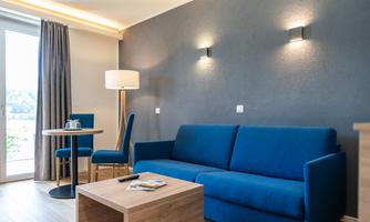 A modern living room with a blue sofa and a wooden table.  
Large windows let in plenty of light.
