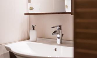 A modern bathroom with an elegant sink and a shiny faucet. On the shelf, there are white candles and a soap dispenser bottle.