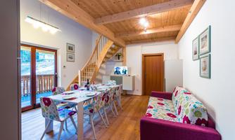 A cozy living and dining area with a wooden table and colorful chairs. The room has large windows that let in plenty of light.