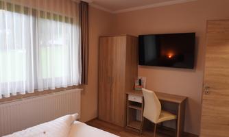 A cozy room with a bed, a workspace, and a television. Large windows provide plenty of natural light.