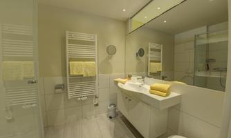 A modern bathroom with a bright design. It features a shower, a sink, and towels in soft colors.