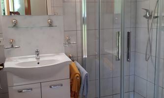 A modern bathroom with a glass shower and bright tiles. The room is well-lit and features a sink with a countertop.