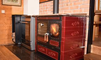 A modern kitchen with a red stove and an oven. The walls are made of wood, creating a cozy atmosphere.