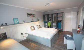A cozy bedroom with two single beds and modern furnishings. The room is bright and friendly with wooden flooring and an open wardrobe.