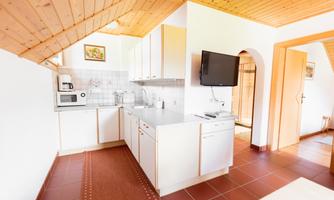A modern kitchen with a wooden ceiling and white cabinets. It is well-equipped with a microwave and a TV.