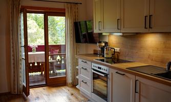 A modern kitchen with wood surfaces and a view of a balcony. Large windows let in plenty of light.