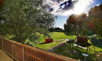A beautiful landscape with lots of green grass and trees. In the background, play facilities and a bright sky can be seen.