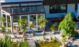 A beautifully designed conservatory with many plants and colorful flower pots. In the background, you can see a well-kept terrace and a small pond.