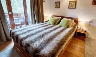 A cozy bedroom with a double bed and light green pillows. Large windows provide a view outside and ensure plenty of light.