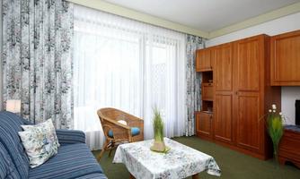 A cozy living space with a blue sofa and a wicker chair. Large windows let in plenty of light and the decor is floral and inviting.