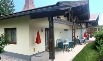 A beautiful house with a garden and a terrace. On the terrace, there are tables and chairs, and there are umbrellas.