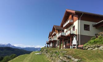 A picturesque cabin landscape in a meadow with a view of the mountains. The sky is clear and blue, perfect for a relaxing stay.