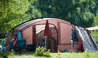 A tent at a campsite, surrounded by trees. There are camping chairs and a sun umbrella.