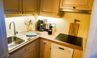 A small, modern kitchen with light cabinets and a sink. On the countertop are a coffee maker and a kettle, as well as a dishwasher and an induction stove.