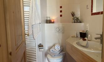 A small, modern bathroom with white tiles and red accents. Towels are neatly stacked, and a candle provides a cozy atmosphere.