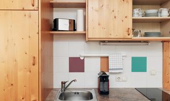 A modern kitchen with wooden cabinets and a stainless steel sink. On the countertop are a coffee machine and dishes.