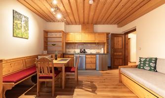 A cozy, well-equipped kitchen with wooden details and plenty of natural light. The space includes a dining area and a comfortable seating corner.