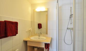 A modern bathroom with a shower cabin and a sink. Red towels and a large mirror complement the decor.