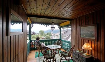 A cozy wooden porch with a table and rattan chairs. In the background, mountains and a clear sky are visible.