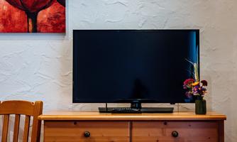 A modern television stands on a wooden dresser. In the background, there is a red painting, and next to it, there is a vase with colorful flowers.