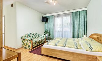 A simple room with a double bed and a cozy couch. The walls are light green, and there is a window with curtains.