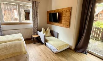 A cozy bedroom with a double bed, a sitting area, and a television on the wall. Plenty of light enters the room through large windows.