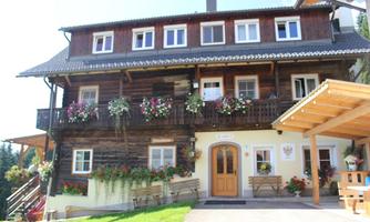 A traditional wooden house with blooming balcony plants. The entrance area is invitingly designed and surrounded by green grass.
