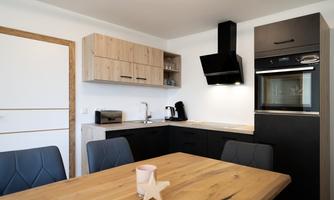 A modern kitchen with wooden and black furniture. The wooden table is in the center, surrounded by elegant chairs.