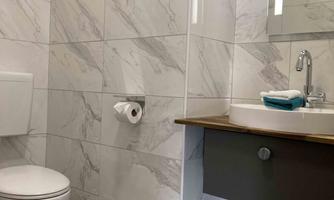 A modern bathroom with marbled wall tiles. It features a toilet, a sink, and a large mirror.