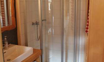 A bathroom with a modern shower and a sink. The walls are light and the floor has dark tiles.