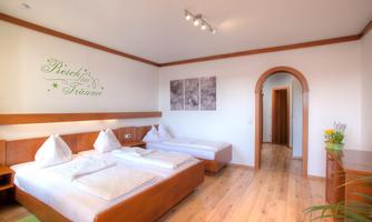 A bright room with two single beds and a double bed. The walls are in neutral colors and feature decorative elements.